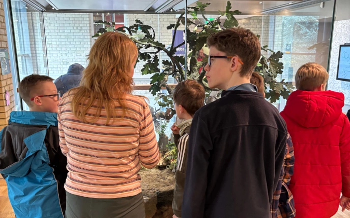 A school group stand in front of the natural history display with a teacher