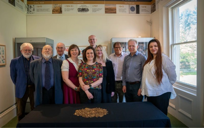 Large group of people posing with pile of coins from Baddow Hoard