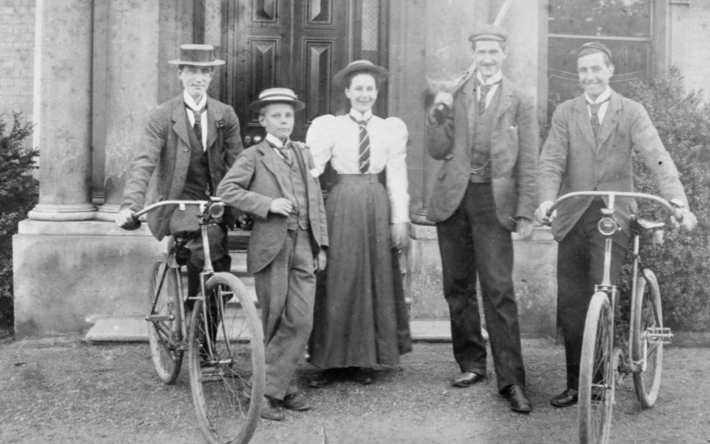 Black and white photo with three men, two with bikes, a woman in a long skirt and a school boy
