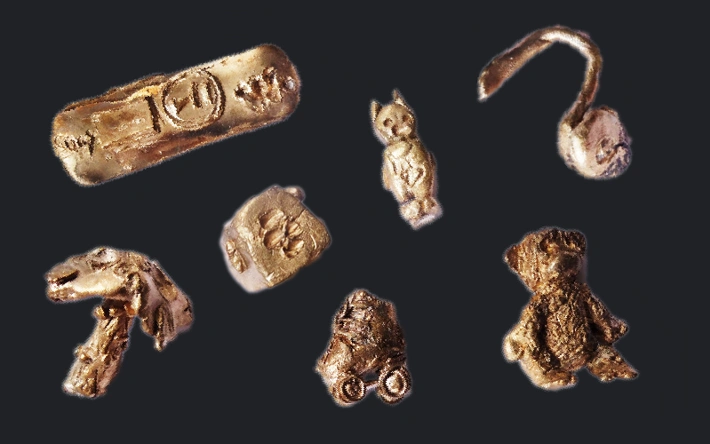 Objects such as a teddy bear and die are cast in bronze and lie against a black background