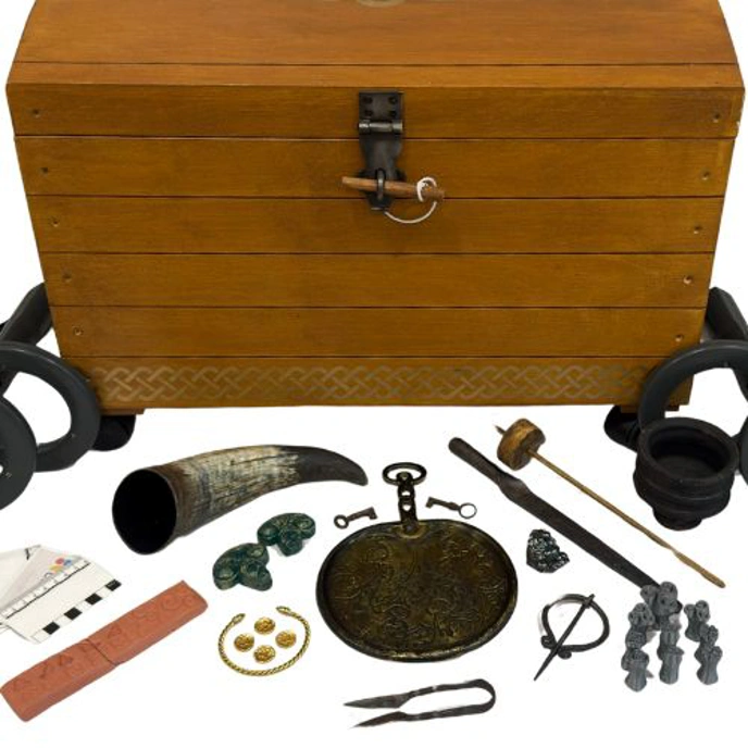 A wooden box with various iron age artefacts and metal detectors laid out in front of it. 