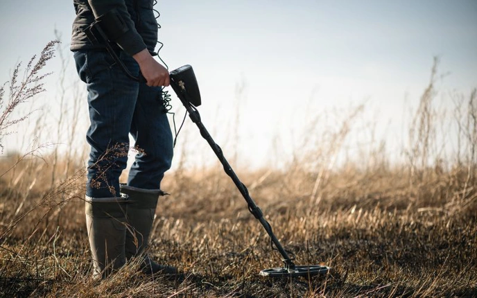 Man wearing wellies using metal detector in field