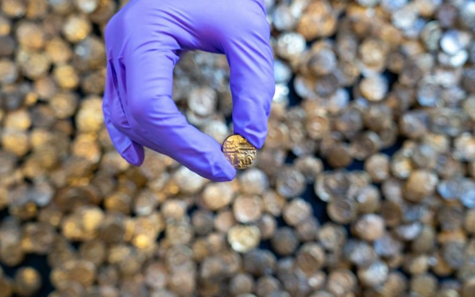 Hand wearing purple glove holding small coin